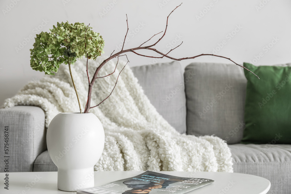 Vase with flowers, tree branch and magazine on table in living room