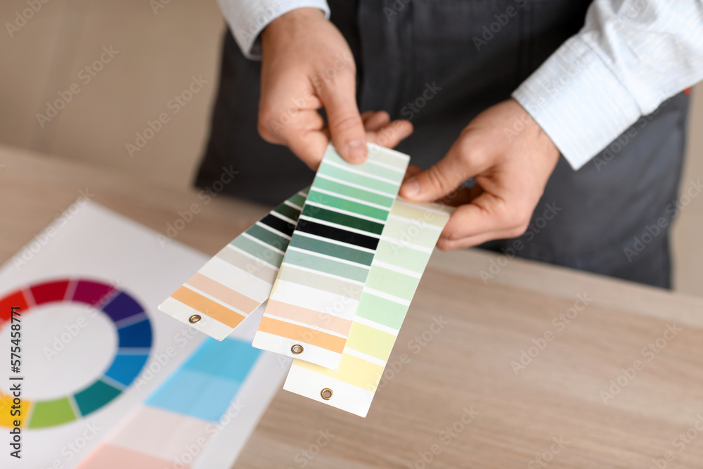 Male painter with color palettes at table in room, closeup