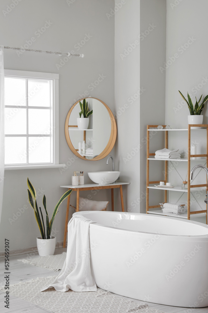 Stylish interior of bathroom with modern bathtub, sink and shelving units with accessories