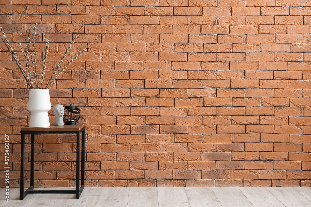 Vase with pussy willow branches and decor on table near brick wall