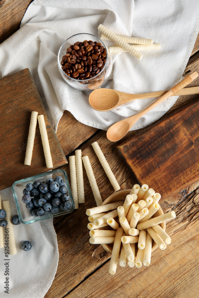 Bowls with delicious wafer rolls, blueberries and coffee beans on wooden table