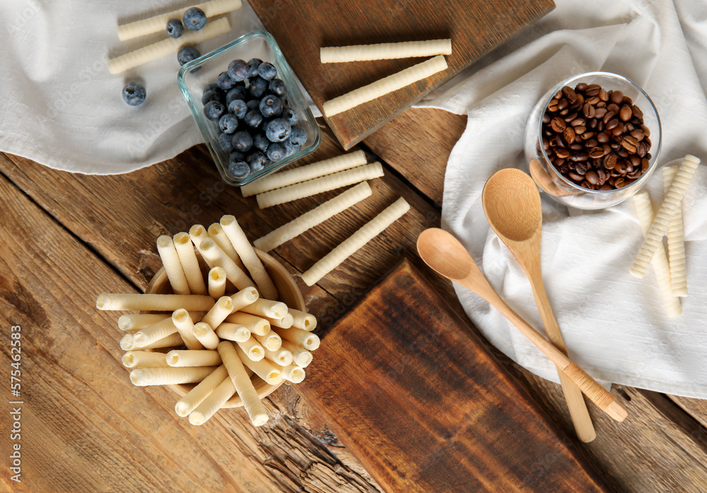 Bowls with delicious wafer rolls, blueberries and coffee beans on wooden table