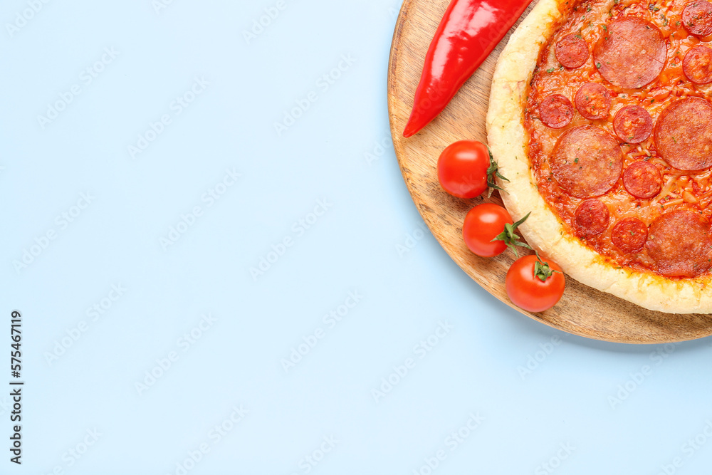 Board with delicious pepperoni pizza, jalapeno peppers and tomatoes on blue background