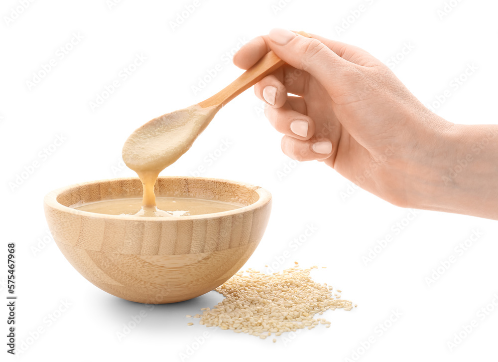 Female hand with bowl of tasty tahini and sesame seeds on white background, closeup