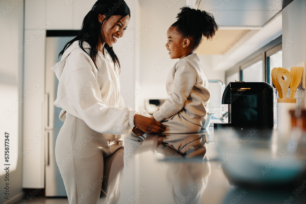 Woman smiling at her daughter who’s sitting on a kitchen counter