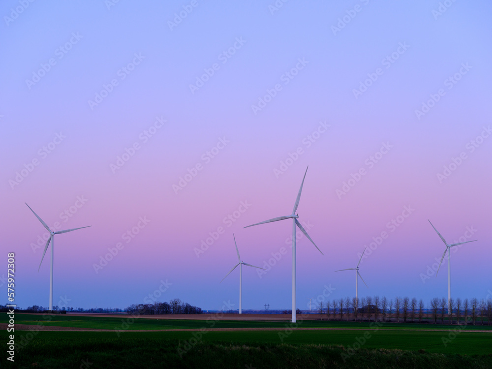 Wind turbines to produce electricity at sunset in a field in France