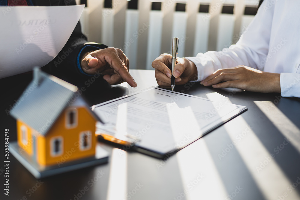 Businessman in suit in his office showing home insurance policy and pointing with a pen where the po