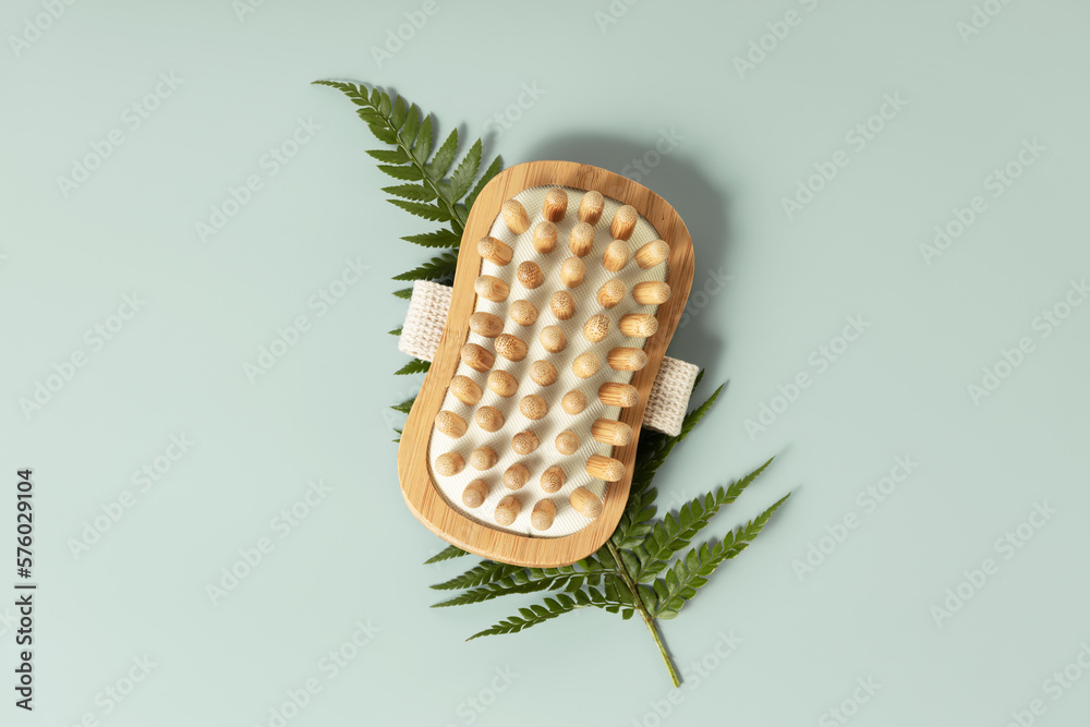 Massage wooden brush with leaves on pastel blue background,