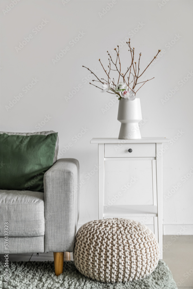 Vase with tree branches and flowers on table in light living room