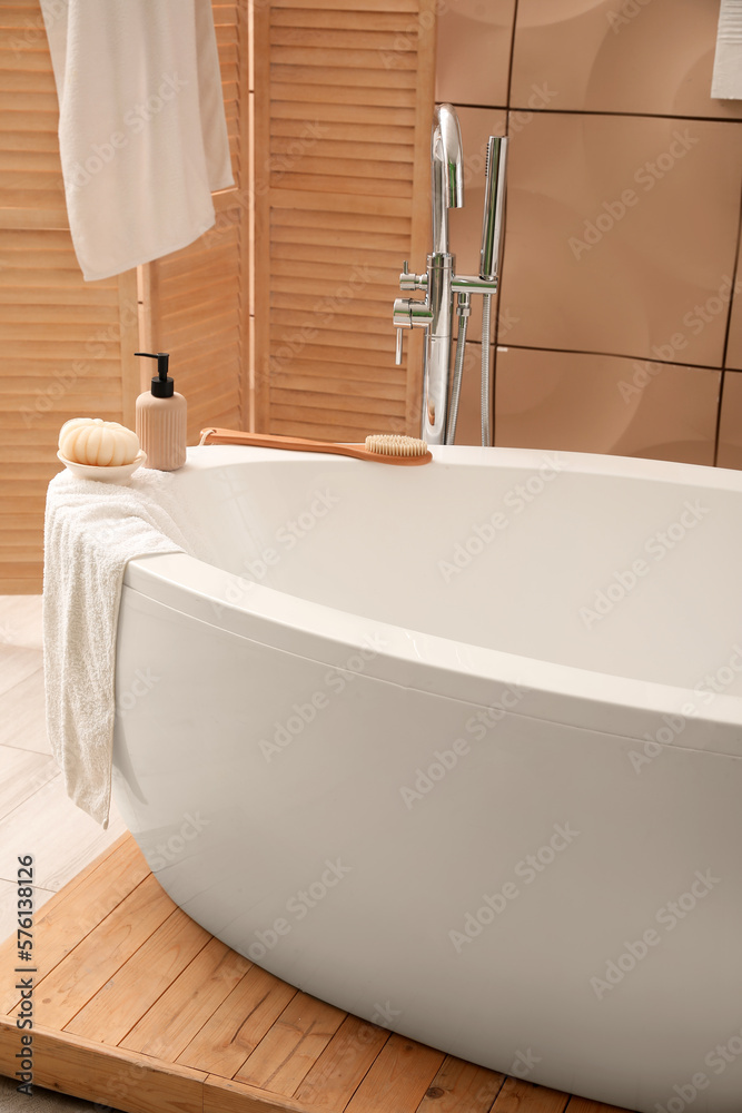 Interior of bathroom with modern bathtub, folding screen and towels