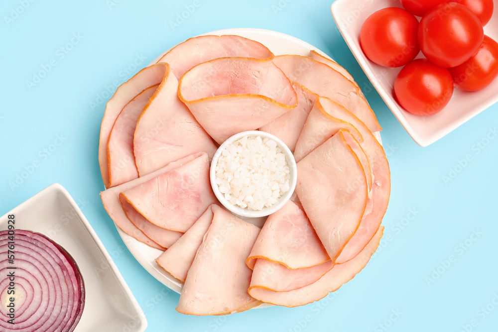 Dishes with slices of tasty ham, sea salt and tomatoes on blue background