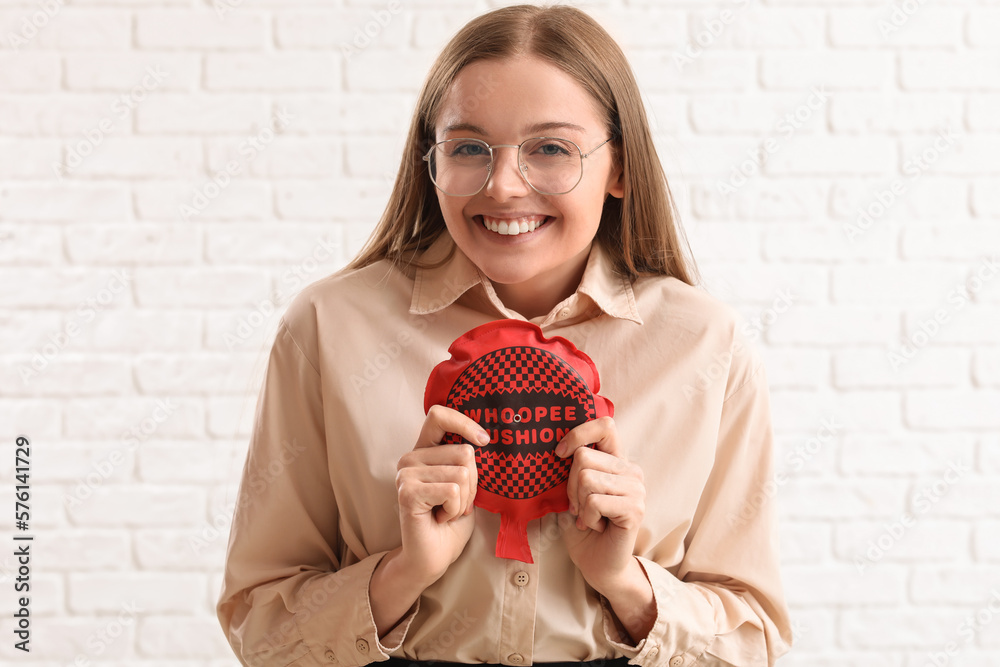 Young woman with whoopee cushion on white brick background. April Fools Day celebration