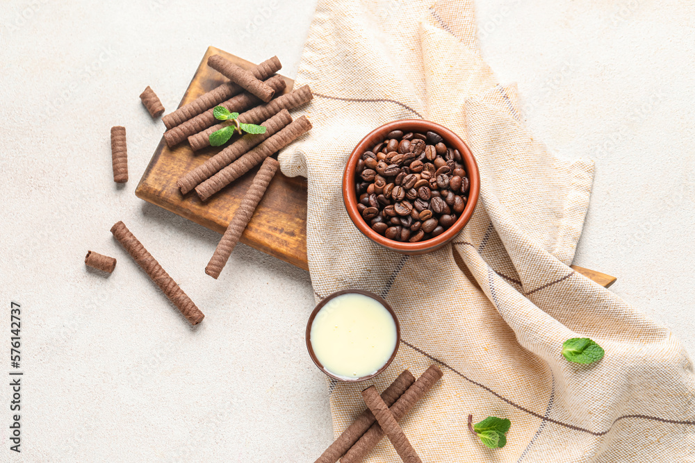 Board with delicious chocolate wafer rolls, coffee beans and condensed milk on white background