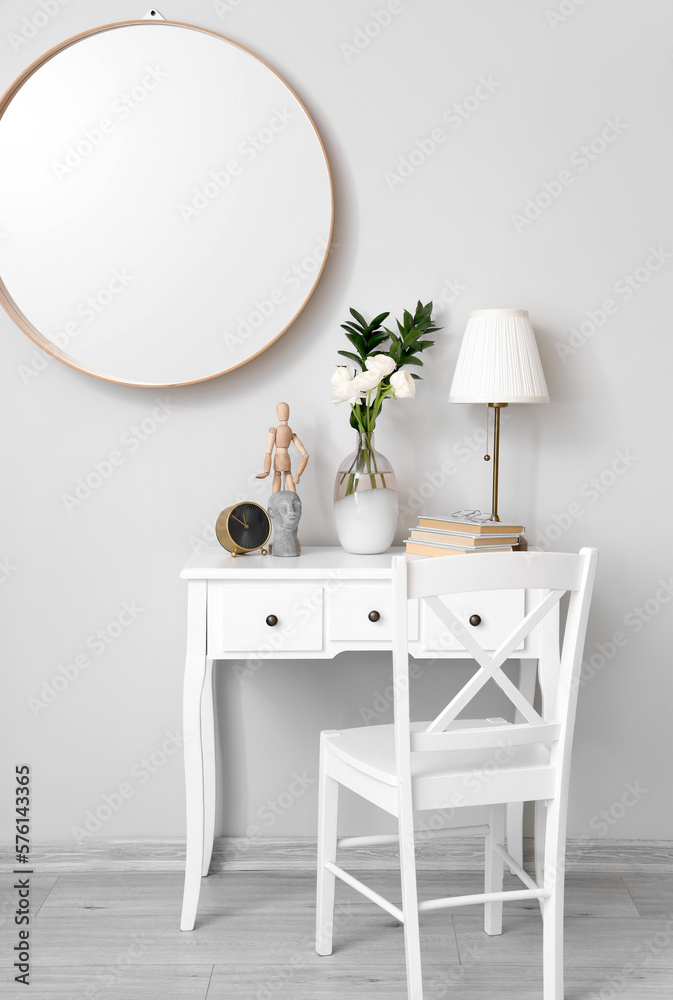 Vase with ranunculus flowers, lamp, alarm clock and decor on table near light wall in room