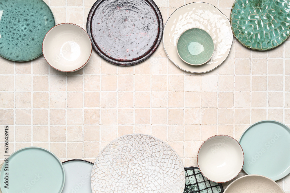 Frame made of clean ceramic plates and bowls on tile background