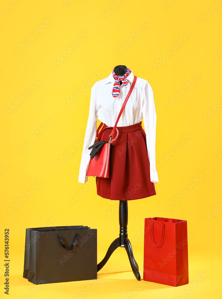 Mannequin with stylish clothes and shopping bags on yellow background