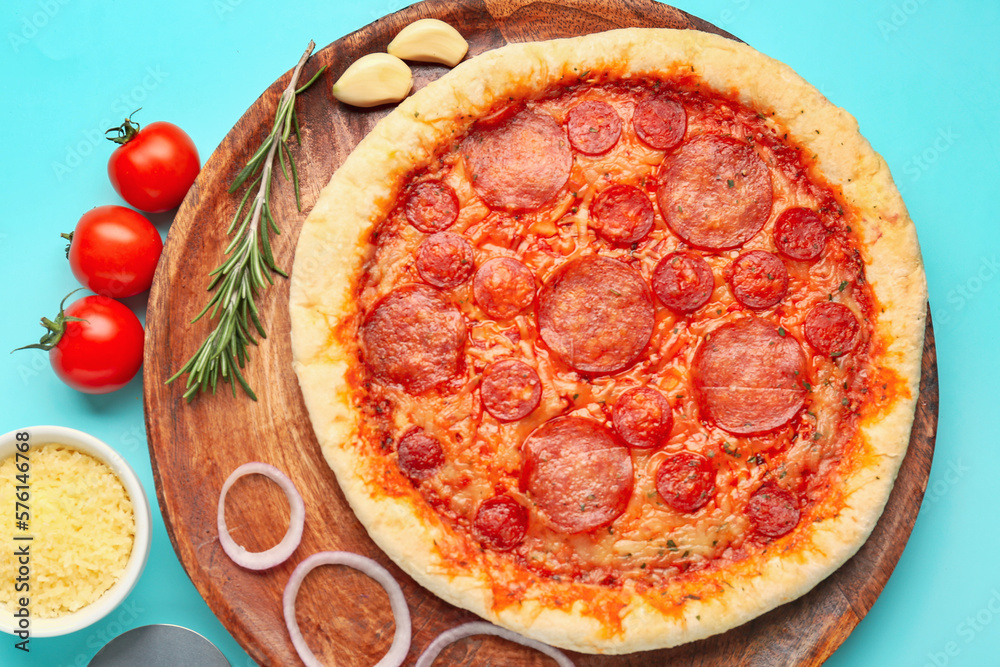 Board with delicious pepperoni pizza and ingredients on turquoise background