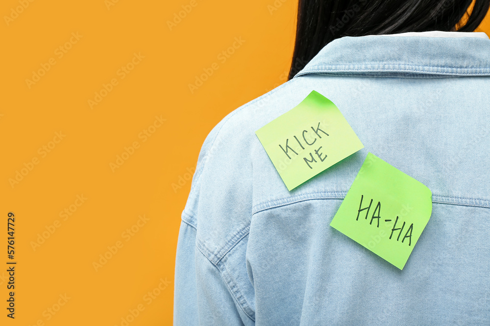 Sticky papers on womans back against orange background, closeup. April Fools Day celebration