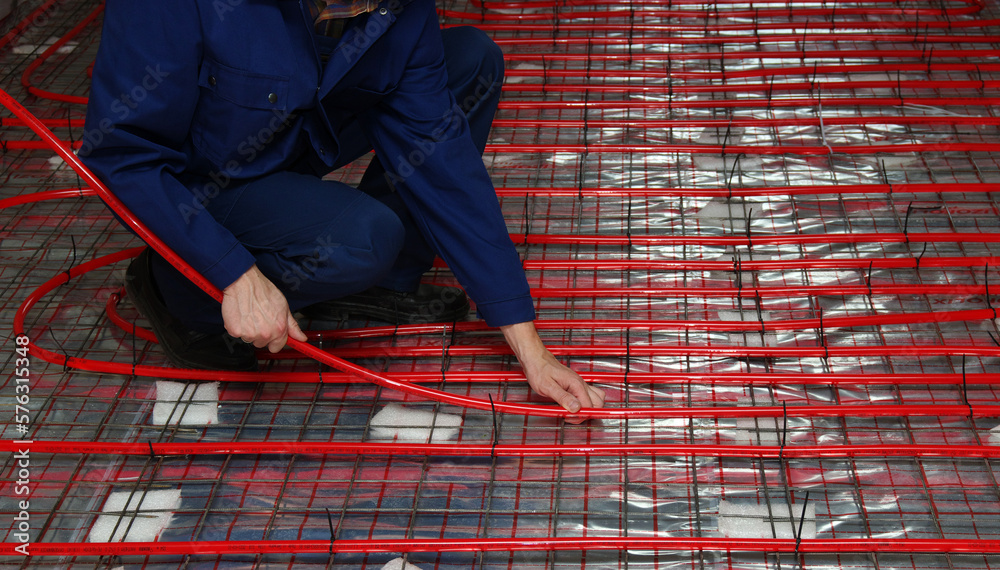 Worker is installing a red pipe for underfloor heating