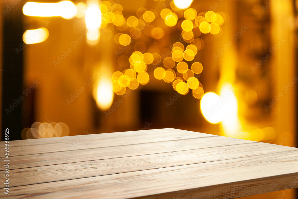 Empty wooden table top on blur light golden bokeh of cafe restaurant, bar in a dark background.