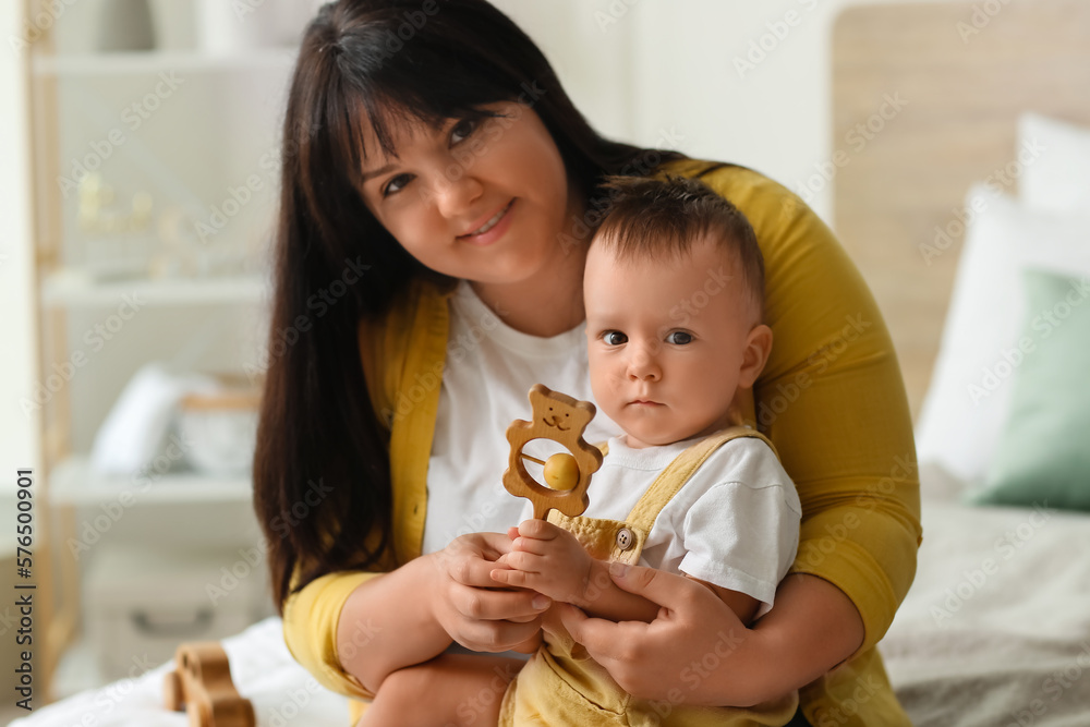 Happy mother with her baby boy and rattle in bedroom