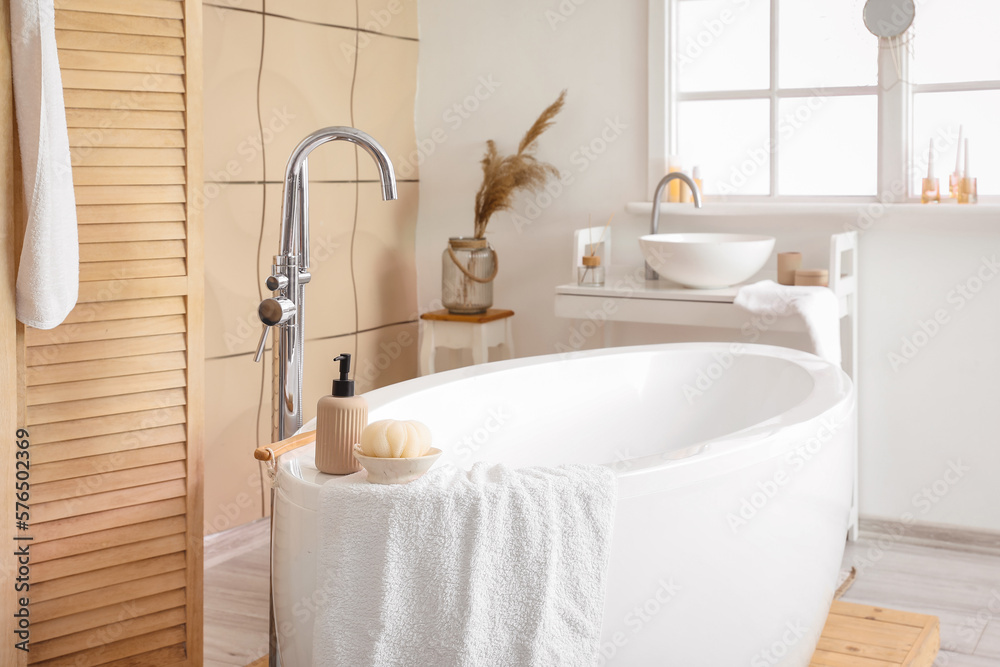 Interior of bathroom with modern bathtub and ceramic sink near window