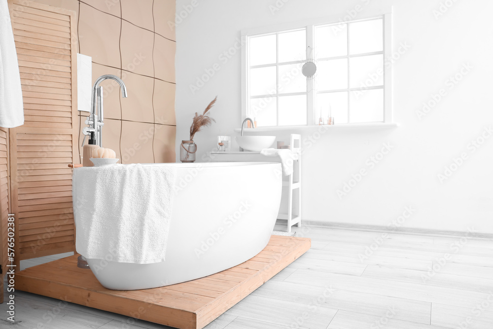 Interior of bathroom with modern bathtub and ceramic sink near window