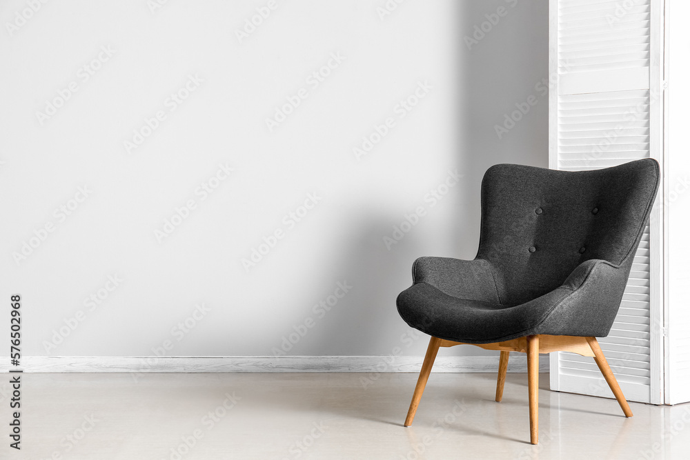 Stylish grey armchair and folding screen near white wall