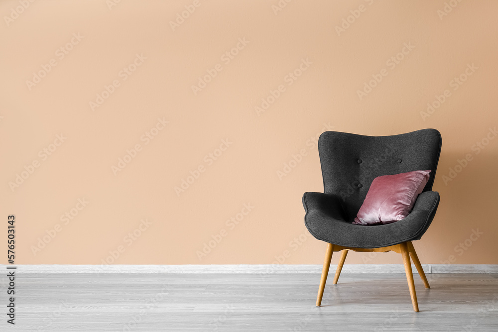 Stylish grey armchair with cushion near beige wall