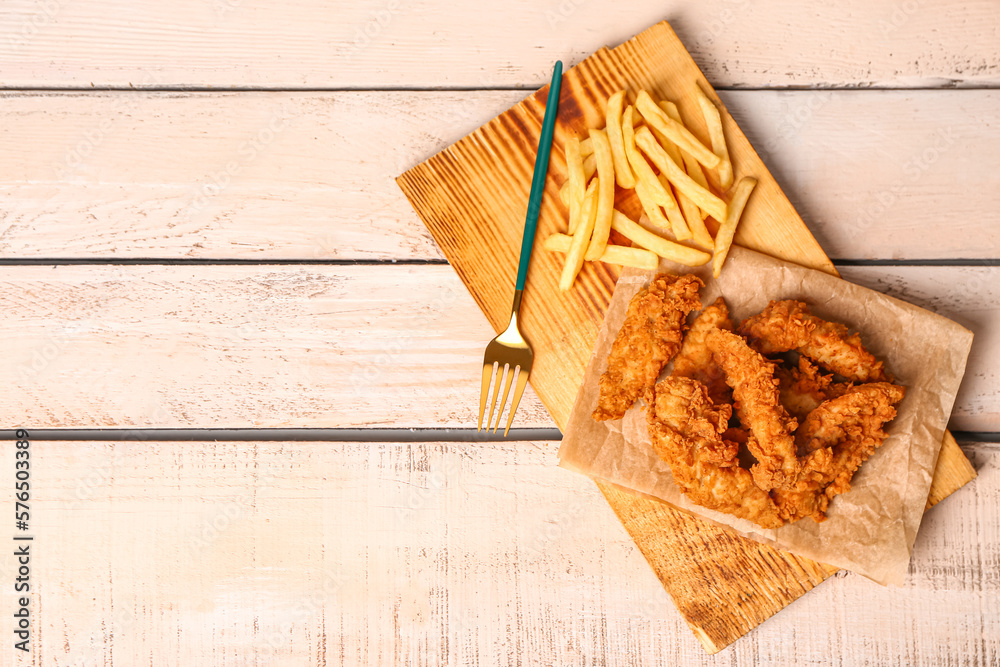 Board with tasty nuggets and french fries on light wooden background