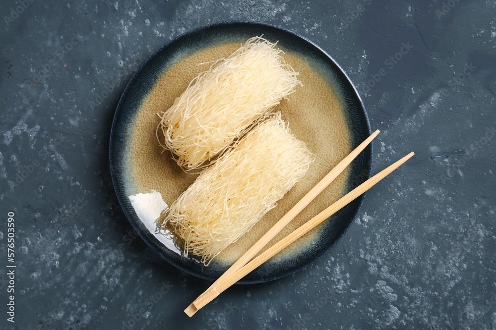 Plate with raw rice noodles and chopsticks on dark background