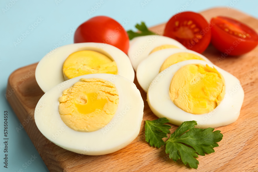 Board with delicious boiled eggs, tomatoes and parsley on blue background