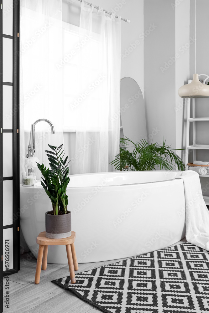 Interior of light bathroom with white bathtub and houseplants