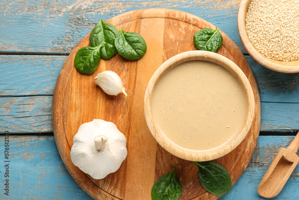 Composition with bowls of tasty tahini, sesame seeds, garlic and spinach on color wooden background,