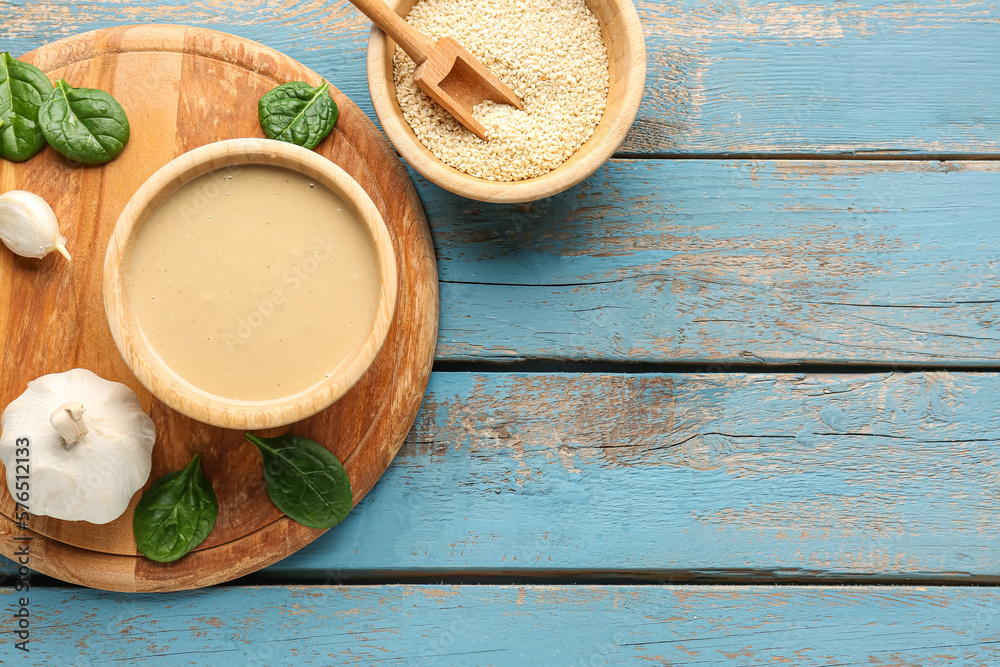 Composition with bowls of tasty tahini, sesame seeds, garlic and spinach on color wooden background