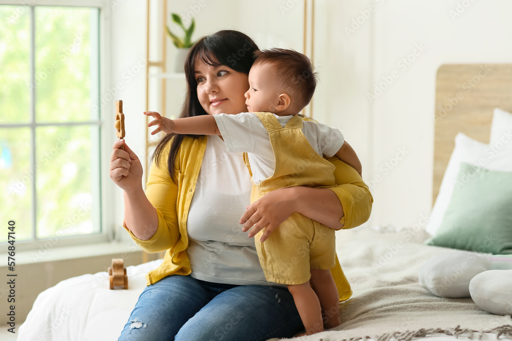 Happy mother with her baby boy and rattle in bedroom