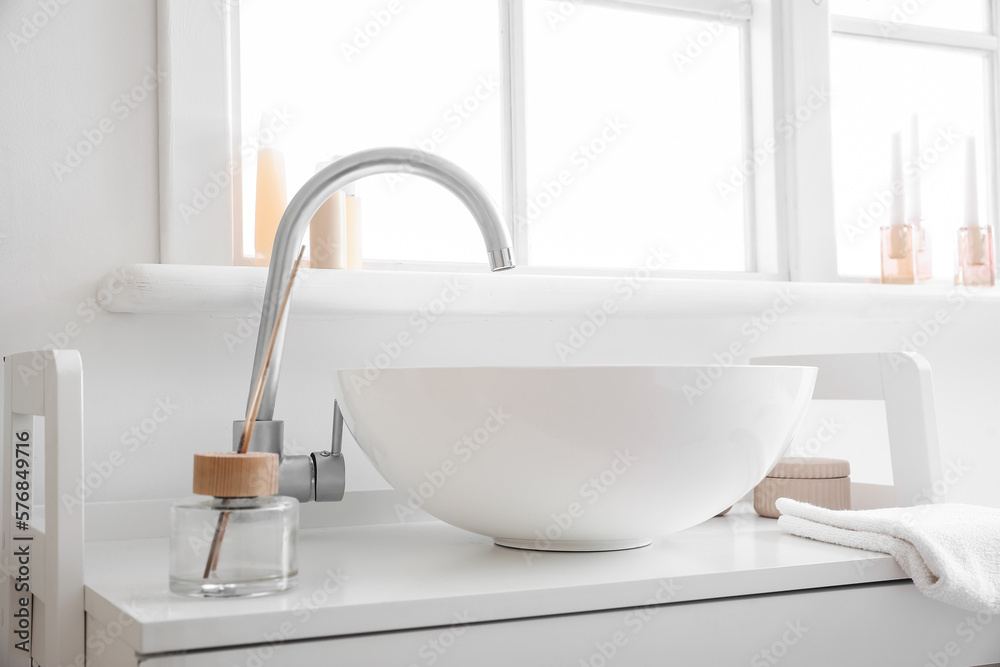 Interior of bathroom with ceramic sink and reed diffuser near window