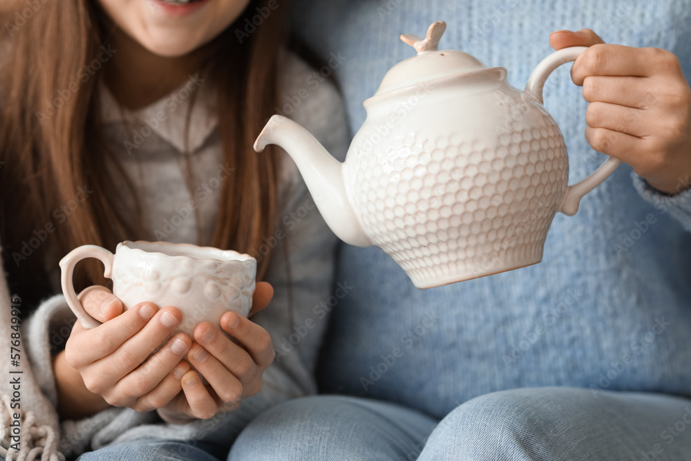 Mother pouring tea into her little daughters cup at home, closeup