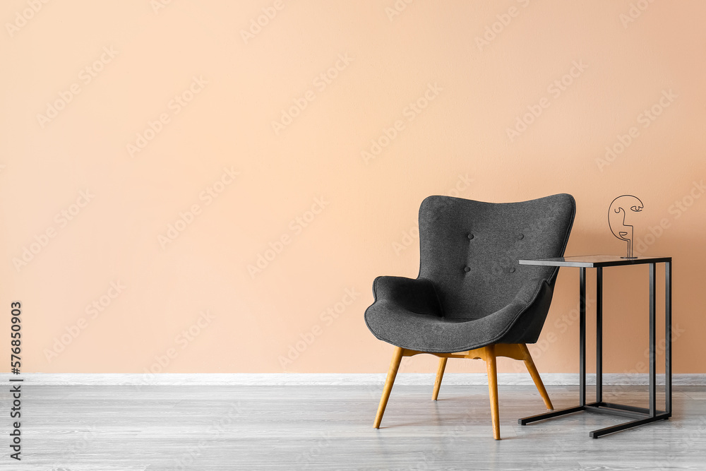 Stylish grey armchair and table near beige wall