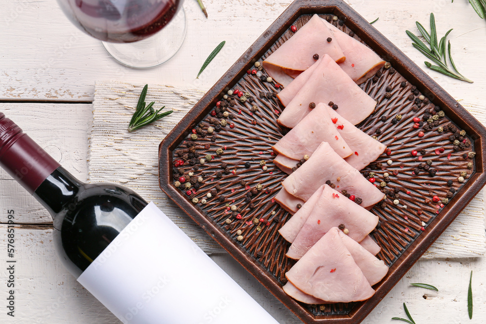 Board with tasty ham slices and bottle of wine on white wooden background