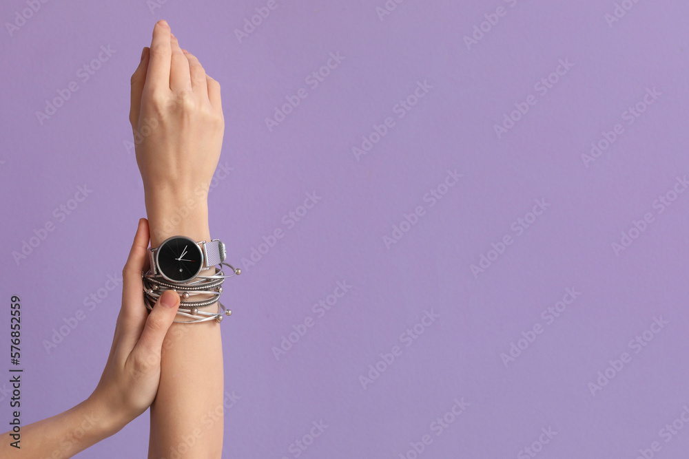 Woman with stylish wristwatch and bracelet on lilac background