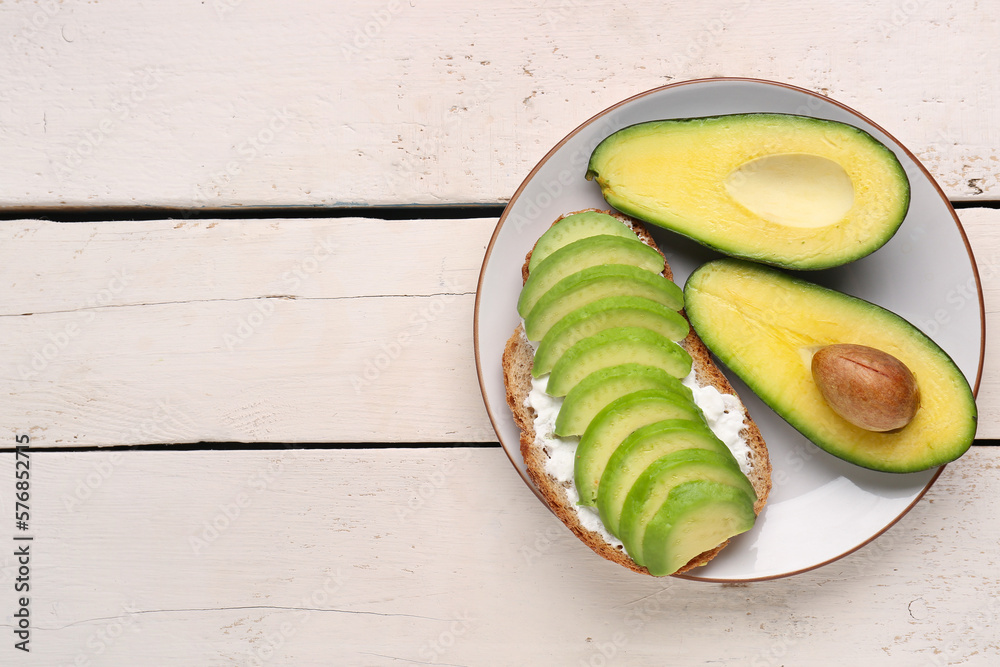 Plate with delicious avocado toast on white wooden background