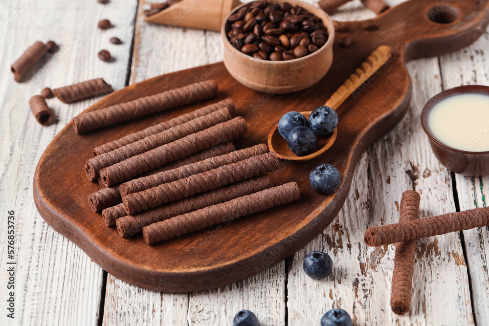 Board with delicious chocolate wafer rolls, coffee beans, condensed milk and blueberries on white wo