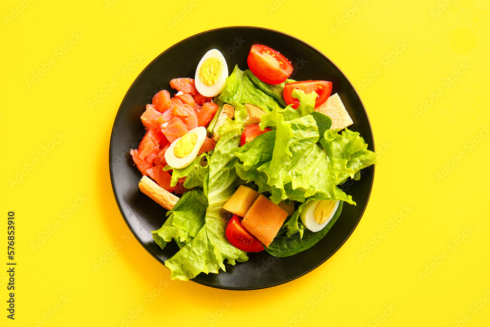 Plate of delicious salad with boiled eggs and salmon on yellow background