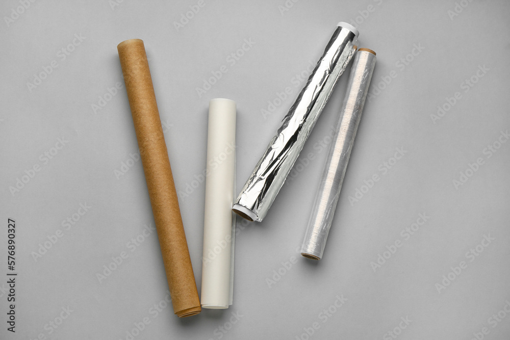 Rolls of aluminium foil, baking paper and food film on grey background