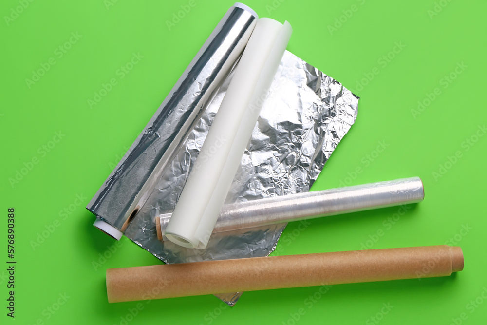 Rolls of aluminium foil, baking paper and food film on green background