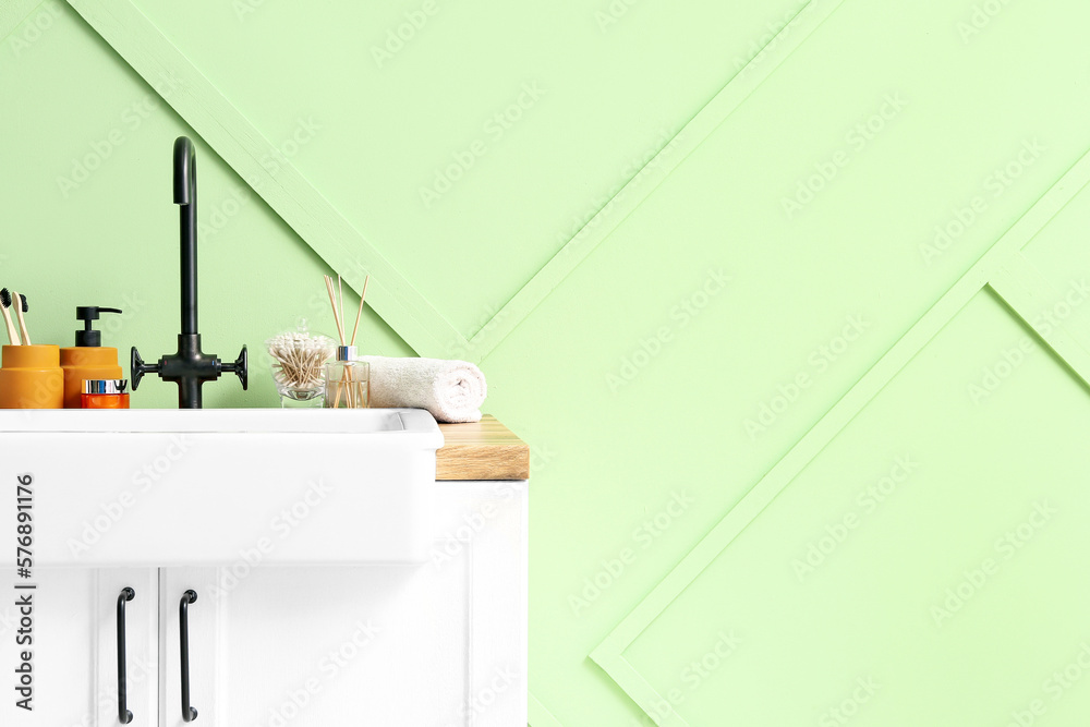 Table with ceramic sink and bath accessories near green wall