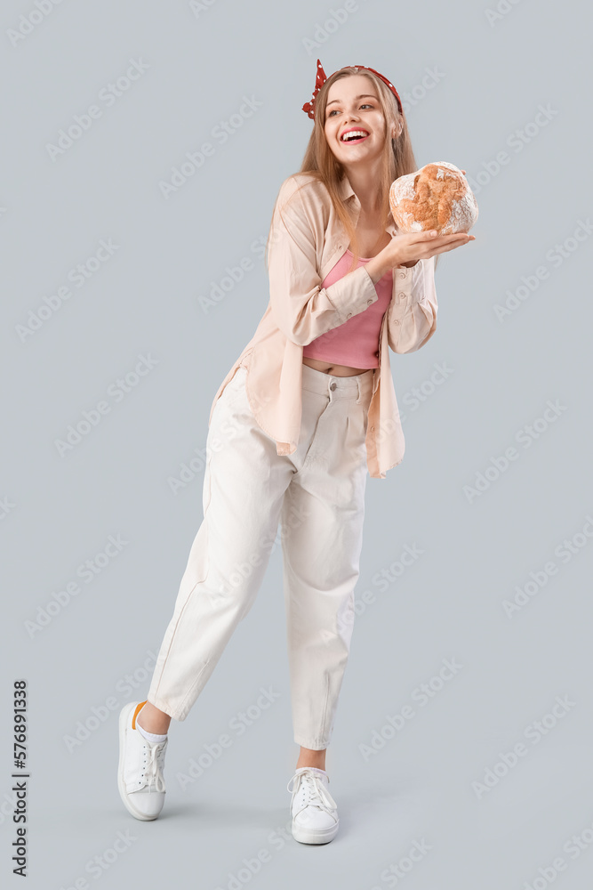 Young woman with fresh bread on grey background