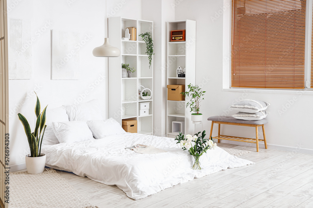 Interior of light bedroom with flowers in vase and houseplants