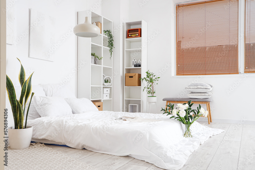 Interior of light bedroom with flowers in vase and houseplants